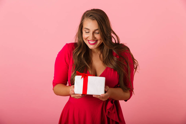 Image of an excited young woman isolated over pink wall background holding gift surprise box. - 写真・画像