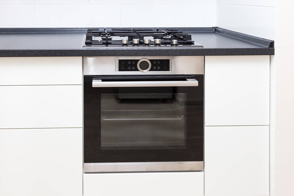 Horno empotrado y gama en cocina blanca con mostrador negro, primer plano
. - Foto, imagen