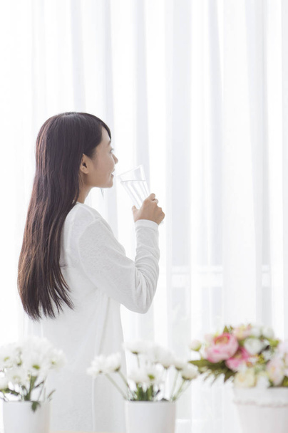 Jovencita sosteniendo un vaso de agua y sonriendo mirando hacia otro lado
 - Foto, Imagen