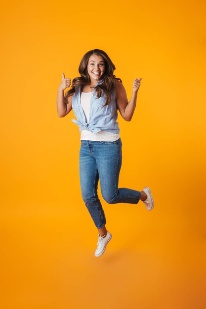Full length portrait of an excited young casual woman jumping isolated over yellow background, celebrating success - Fotografie, Obrázek