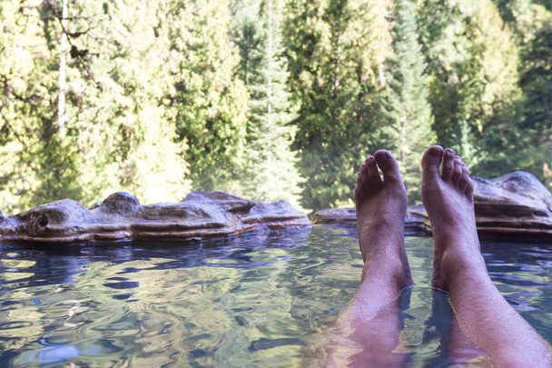 расслабляющий горячие минеральные бассейны в окружении леса в горах Орегона с моими ногами в рамке толкая мою точку зрения
 - Фото, изображение