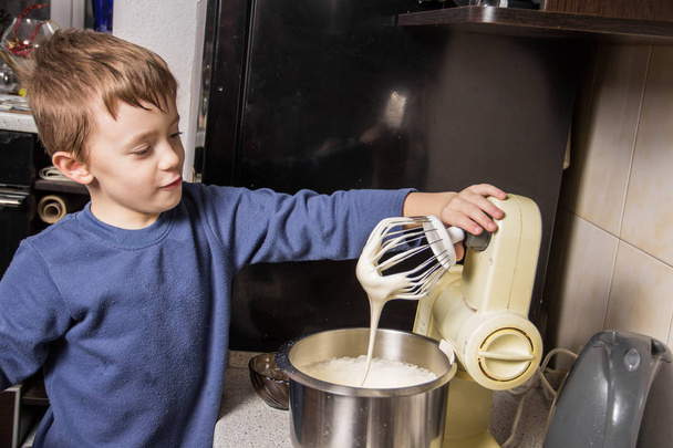 Chłopiec w kuchni wyrabia ciasto na babeczki w mikserze, Dodawanie składników - Zdjęcie, obraz