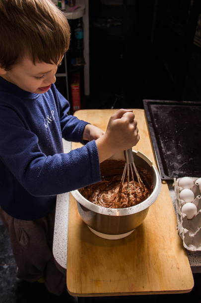 台所の少年は、ミキサーでカップケーキの生地を練り、成分を追加します。 - 写真・画像