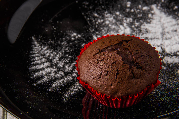 Chocolate muffins on a dark background with a twig decoration painted with icing sugar - Photo, Image