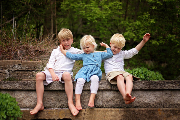 Tři roztomilé děti představují pro portrét venku, ale sestřička je tlačí její velké bratry pryč. - Fotografie, Obrázek