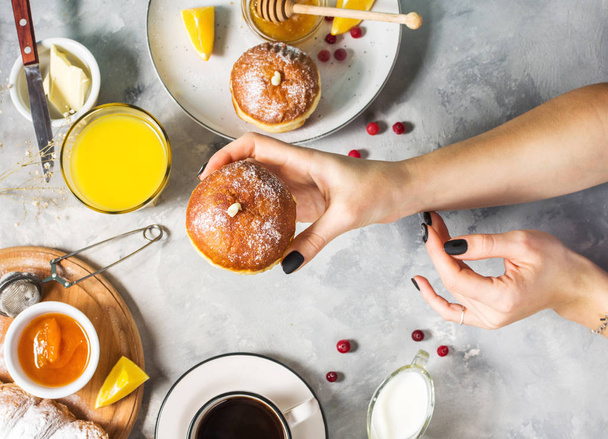 Les mains féminines tiennent donut. Petit déjeuner servi avec café, jus d'orange, croissants et fruits sur fond de béton. Vue du dessus
 - Photo, image
