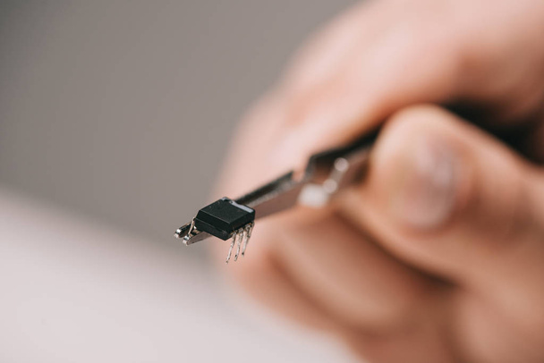 Ausgeschnittene Ansicht einer Pinzette mit Mikrochip-Hand des Menschen auf grauem Hintergrund - Foto, Bild