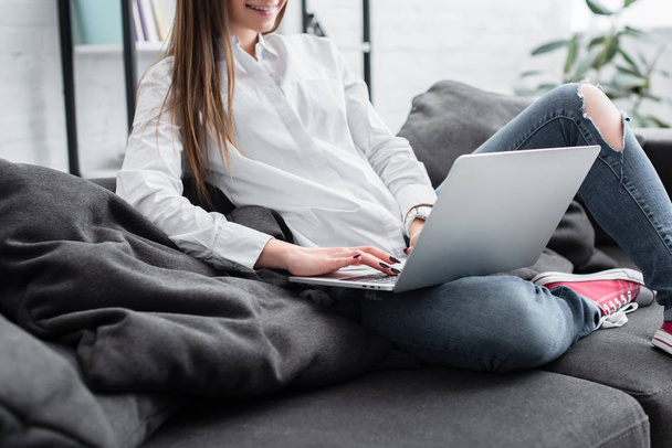 cropped view of girl sitting on couch and using laptop in living room - Photo, Image