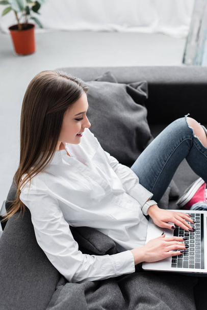 attractive girl sitting on couch and using laptop in living room - Fotografie, Obrázek
