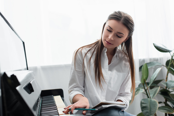 beautiful girl with notebook playing piano and composing music at home - Photo, Image