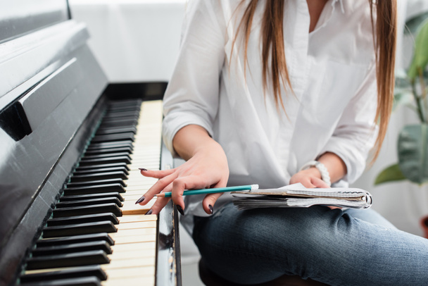 vista recortada de chica en camisa blanca con portátil tocando el piano y componiendo música en casa
 - Foto, imagen