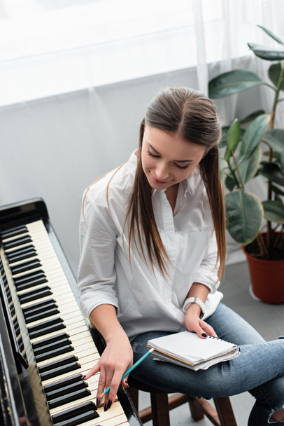 attractive girl with notebook playing piano and composing music at home - Фото, изображение