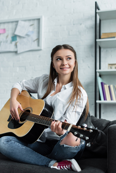 szép mosolygó lány ül, és gitározni nappali - Fotó, kép