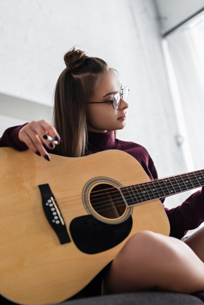 beautiful girl sitting, holding marijuana joint and playing guitar at home - Fotó, kép