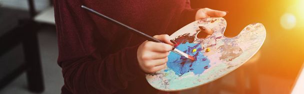 vista parcial de niña sosteniendo pincel con paleta y pintura en casa con retroiluminación
 - Foto, Imagen