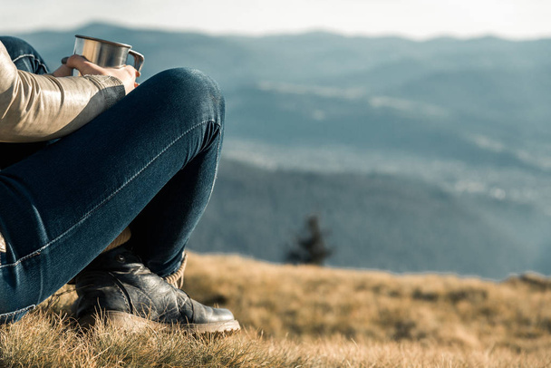 menina com uma xícara de metal senta-se em um fundo de montanhas
 - Foto, Imagem