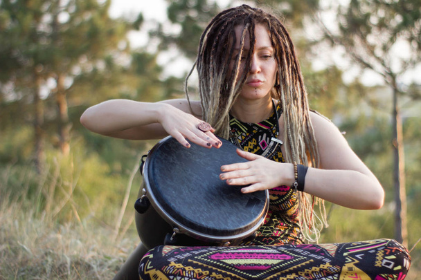 gyönyörű fiatal nő hippi sámán játszik djembe, és a tánc vad táncok naplementekor - Fotó, kép