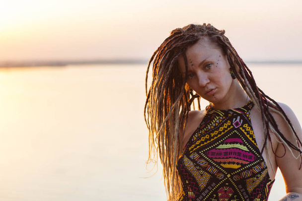 Portrait of young beautiful hippie woman with dreadlocks at sunset. Posing - Photo, Image