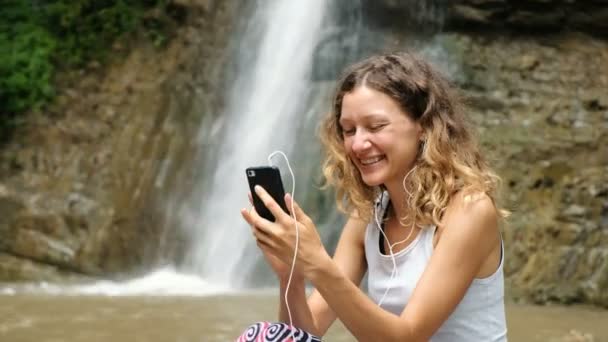Mujer ondea su teléfono, habla en auriculares a través de un enlace de vídeo, y muestra una cascada
 - Imágenes, Vídeo