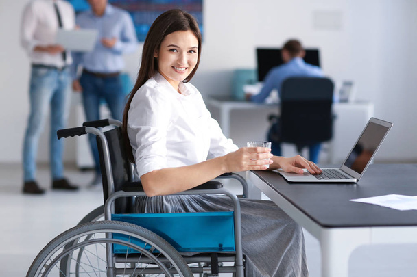 Young woman in wheelchair at workplace - Fotoğraf, Görsel
