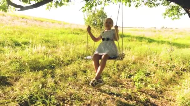 Fille heureuse avec les cheveux longs balançant sur balançoire sous chêne d'été dans une robe blanche et rit
. - Séquence, vidéo