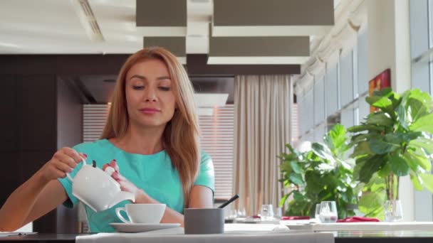 Linda mulher feliz derramando chá em sua xícara, desfrutando de café da manhã no restaurante
 - Filmagem, Vídeo