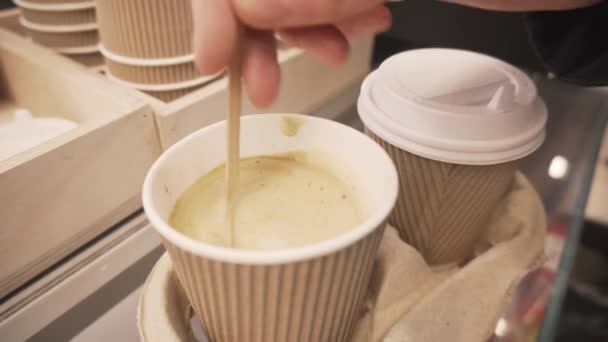 Mano revuelve azúcar con cuchara en taza desechable de café con leche de soja y cubrirlo con tapa de plástico
. - Metraje, vídeo