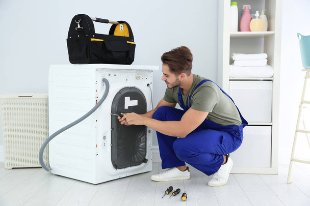 Young handyman fixing washing machine at home. Laundry day - Фото, изображение