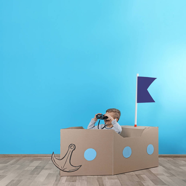 Cute little boy playing with cardboard ship near color wall. Space for text - Fotoğraf, Görsel