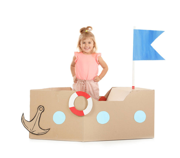 Cute little girl playing with cardboard ship on white background - Fotoğraf, Görsel