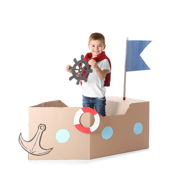 Cute little boy playing with cardboard ship on white background - Foto, Imagem