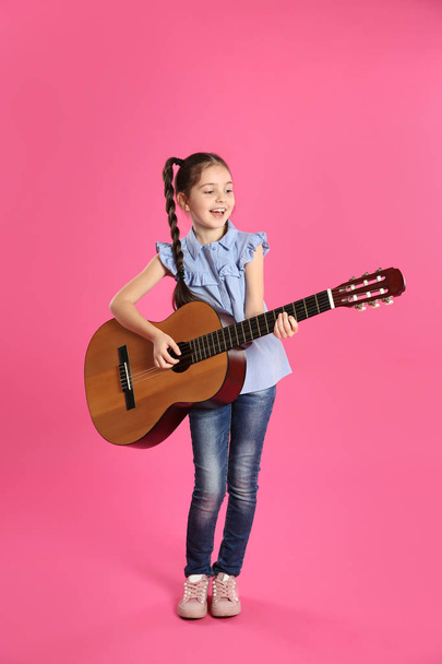 Cute little girl playing guitar on color background - Фото, изображение