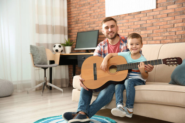 Father teaching his little son to play guitar at home - Фото, изображение