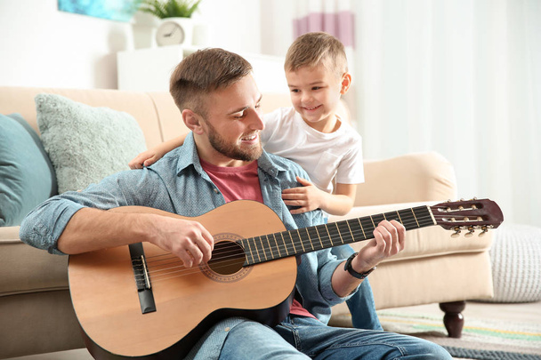 Father playing guitar for his son at home - Fotó, kép