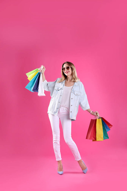 Beautiful young woman with shopping bags on color background - Foto, afbeelding