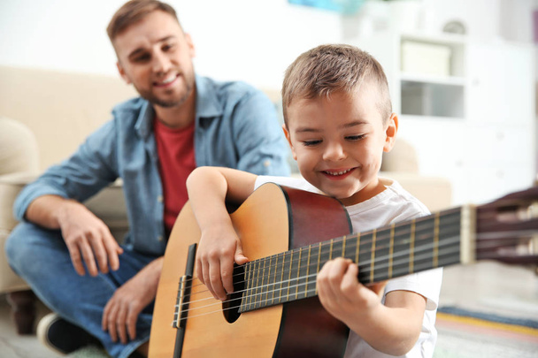 Father watching his son playing guitar at home - Foto, imagen