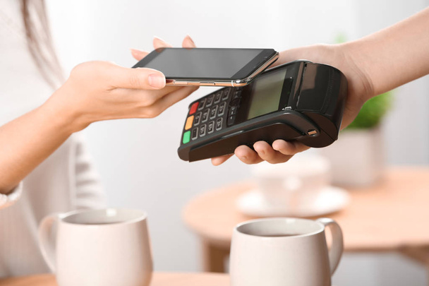 Frau nutzt Terminal für kontaktloses Bezahlen mit Smartphone im Café - Foto, Bild