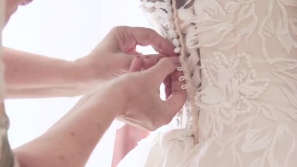 Tlačítka na bílých šatech jsou upevněny na nevěstu na svatbě. Tlačítko nahoru korzet - Záběry, video
