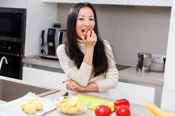 Photo of young brunette biting apple while standing at table with vegetables and fruits - Foto, Imagem
