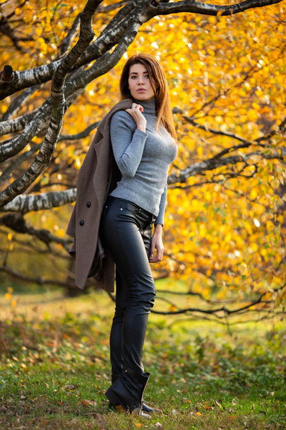Photo of young brunette with coat on her shoulder in autumn forest - Φωτογραφία, εικόνα