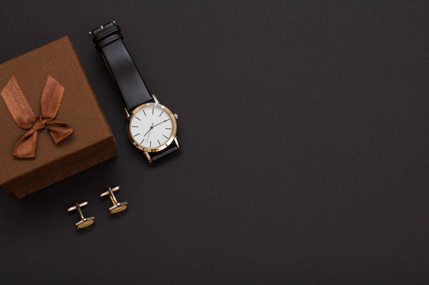 Caixa de presente, relógio com uma pulseira de couro preto e abotoaduras em um fundo preto. Acessórios para homens. Vista superior
. - Foto, Imagem