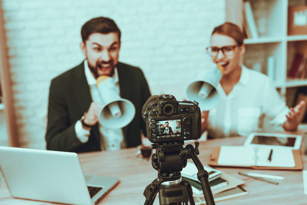 Bloggers Makes a Video. Bloggers is Young Man and Woman. Video About a Business. Camera Shoots a Video. Gadgets and Supplies on Table. People Screaming into a Megaphones. People in Studio Interior. - 写真・画像
