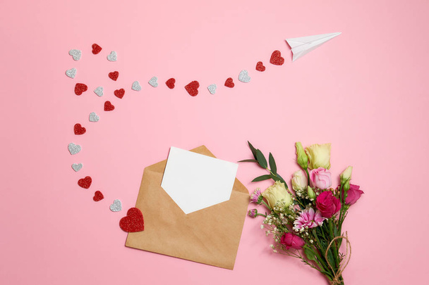 Valentines day composition : bouquet of flowers with ribbon bow, kraft envelope with blank white card for your text, airplane with path made of heart shaped valentine cards. Love concept, send message - Photo, image