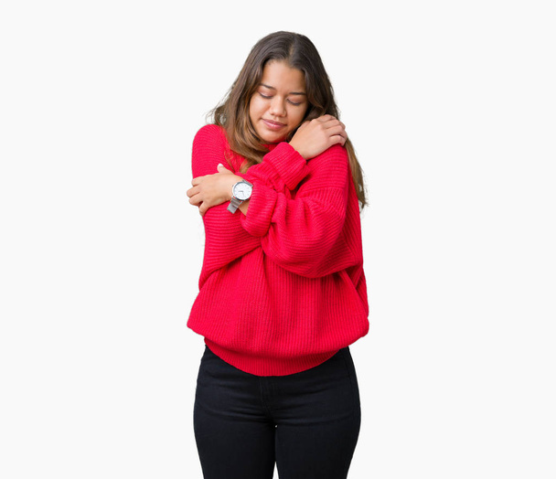 Mujer morena hermosa joven vistiendo suéter rojo de invierno sobre un fondo aislado abrazándose feliz y positivo, sonriendo confiado. Amor propio y cuidado personal
 - Foto, imagen