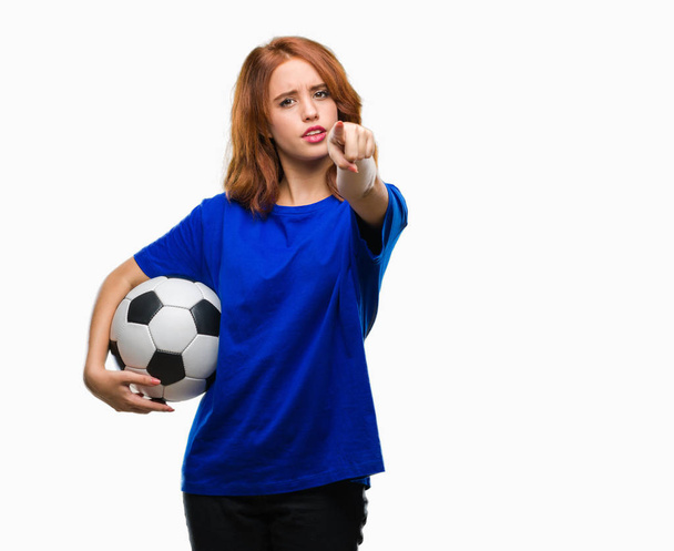 Молодая красивая женщина на изолированном фоне, держа футбольный мяч указывая пальцем на камеру и на вас, знак руки, позитивный и уверенный жест спереди
 - Фото, изображение