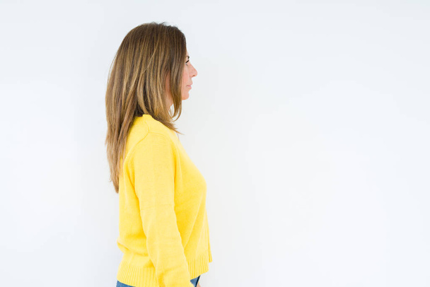 Beautiful middle age woman wearing yellow sweater over isolated background looking to side, relax profile pose with natural face with confident smile. - Photo, Image