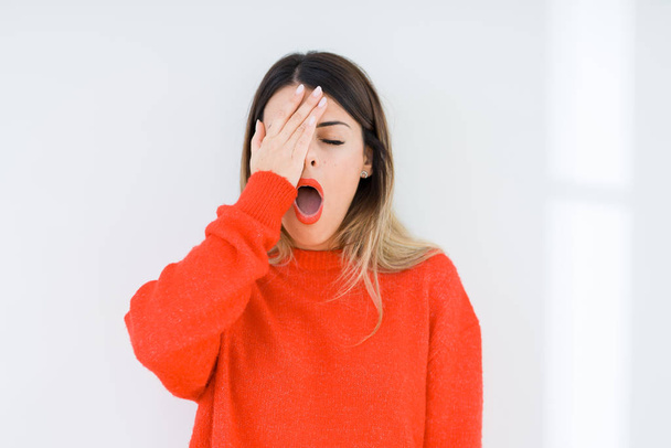 Jonge vrouw dragen casual rode trui over geïsoleerde achtergrond geeuwen moe die betrekking hebben op halve gezicht, ogen en mond met de hand. Gezicht pijn in pijn. - Foto, afbeelding