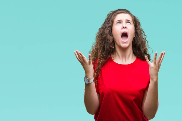 Beautiful brunette curly hair young girl wearing casual look over isolated background crazy and mad shouting and yelling with aggressive expression and arms raised. Frustration concept. - Photo, Image