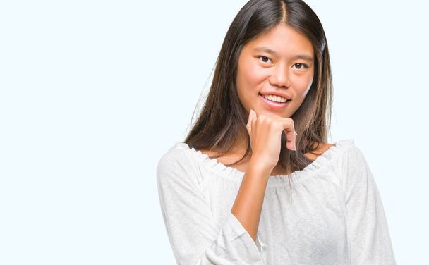 Młoda Azjatka kobieta na białym tle patrząc pewny siebie na aparat z uśmiechem z skrzyżowanymi rękami i ręką uniesioną do góry na podbródek. Myślenie pozytywne. - Zdjęcie, obraz