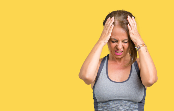Beautiful middle age woman wearing sport clothes over isolated background suffering from headache desperate and stressed because pain and migraine. Hands on head. - Photo, Image